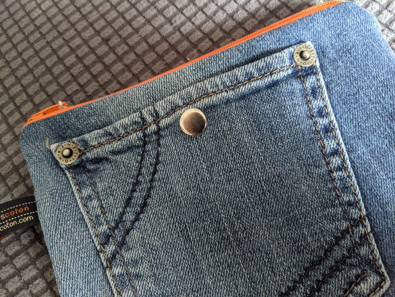 May include: A blue denim pouch with a large pocket and orange trim. The pouch has two silver metal rivets.