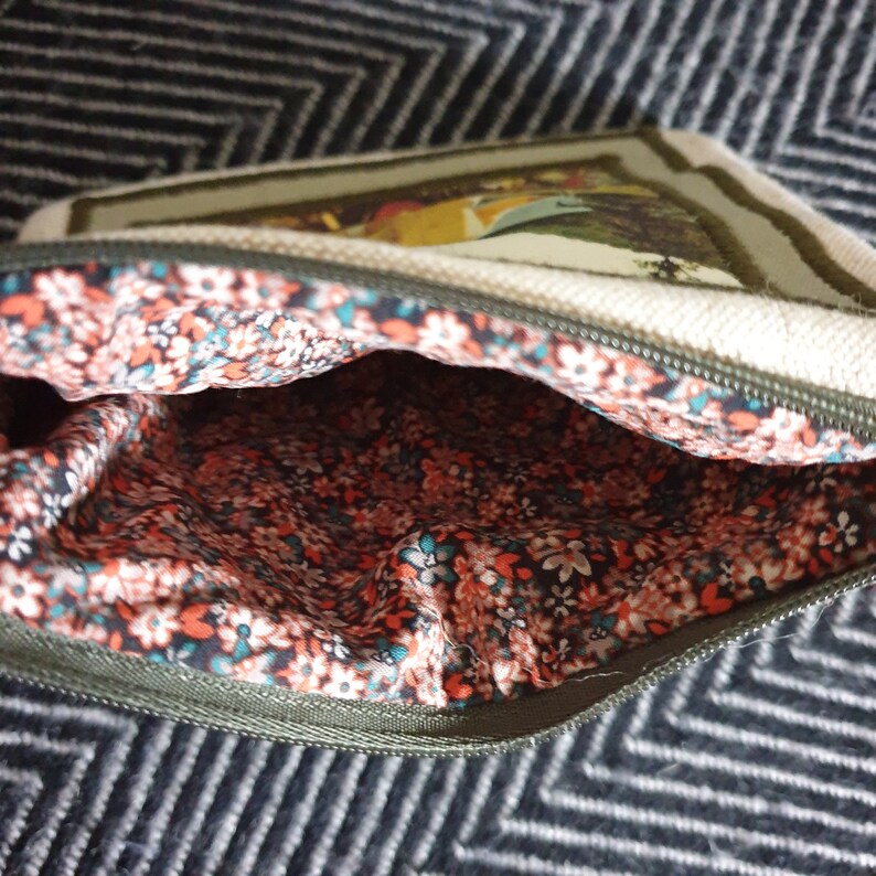 May include: A small, zippered pouch with a floral print lining. The pouch is made of a beige canvas material and has a green trim. The pouch is open, revealing the floral lining.