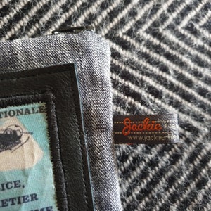 May include: A black and gray fabric wallet with a black leather trim and a small black and white label that says "Jackie" and "www.jackie.fr".
