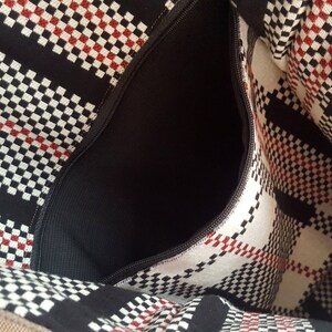 May include: A black and white checkered fabric bag with a red accent. The bag has a zippered pocket on the inside.