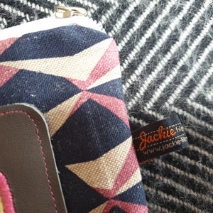 May include: A small zippered pouch with a geometric pattern in shades of pink, white, and blue. The pouch has a brown leather flap with a zipper closure. The pouch has a label that reads "Jackie file www.jackie.nl".