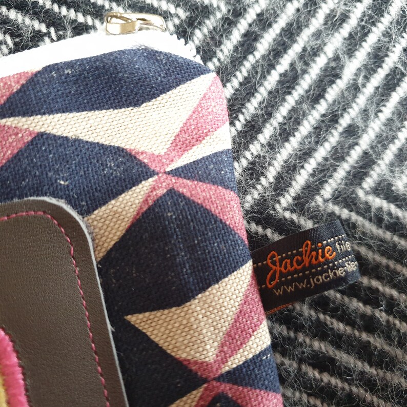 May include: A small zippered pouch with a geometric pattern in shades of pink, white, and blue. The pouch has a brown leather flap with a zipper closure. The pouch has a label that reads "Jackie file www.jackie.nl".