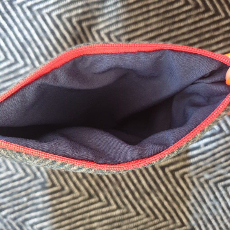 May include: A small zippered pouch with a red zipper and a navy blue lining. The pouch is made of a tweed fabric with a herringbone pattern.