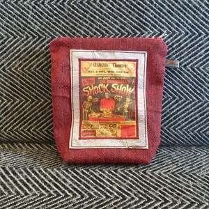 Op de afbeelding: Rode ritszak met een vintage poster van een "Shock Show" met een skelet en een man in een rood shirt. De poster luidt "Dr. Brundell's Shock Show" en "Paramount Theatre".