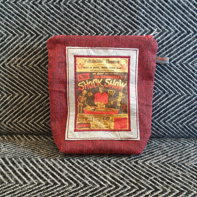 Op de afbeelding: Rode ritszak met een vintage poster van een "Shock Show" met een skelet en een man in een rood shirt. De poster luidt "Dr. Brundell's Shock Show" en "Paramount Theatre".