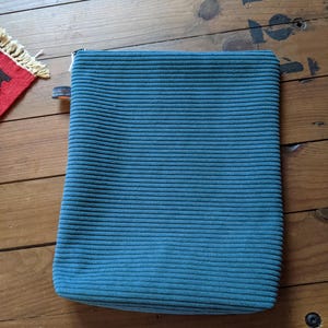 Peut inclure: Une pochette zipp&eacute;e en velours c&ocirc;tel&eacute; bleu sarcelle. La pochette est pos&eacute;e &agrave; plat sur une surface en bois.