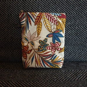 May include: A white zippered pouch with a colorful floral pattern. The pattern features red, yellow, blue, and white flowers and leaves.