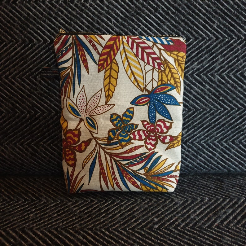 May include: A white zippered pouch with a colorful floral pattern. The pattern features red, yellow, blue, and white flowers and leaves.