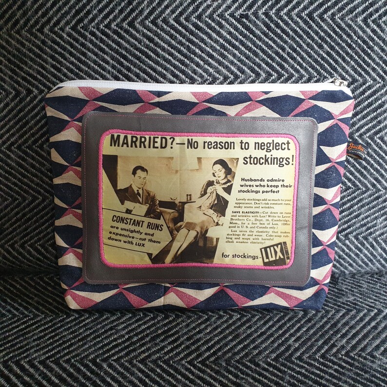 May include: A gray and pink patterned fabric pouch with a zipper closure. The pouch features a vintage advertisement for LUX soap, with the text "MARRIED? - No reason to neglect stockings!" and "Husbands admire wives who keep their stockings perfect."