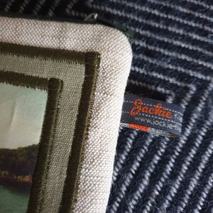 May include: A white canvas zippered pouch with a green embroidered border and a brown label that says "Jackie" with the website "www.jackie.fr".