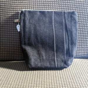 K&ouml;nnte beinhalten: Eine schwarze Rei&szlig;verschlusstasche mit einem wei&szlig;en Rei&szlig;verschluss. Die Tasche ist aus einem weichen, strukturierten Stoff.