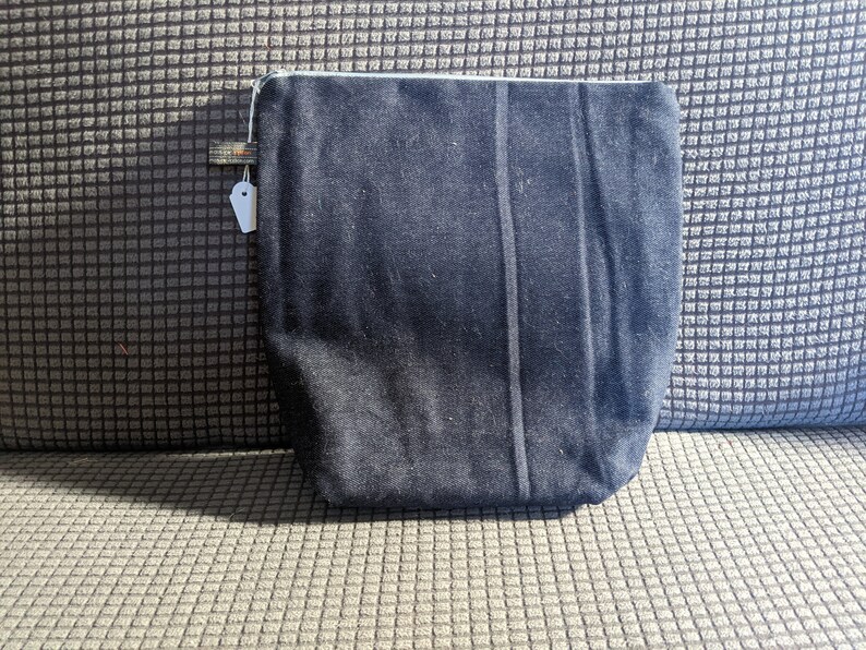 K&ouml;nnte beinhalten: Eine schwarze Rei&szlig;verschlusstasche mit einem wei&szlig;en Rei&szlig;verschluss. Die Tasche ist aus einem weichen, strukturierten Stoff.