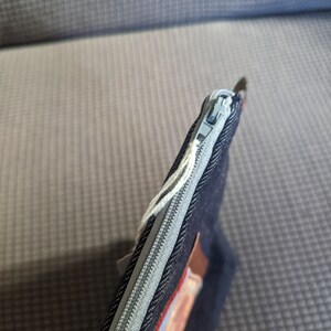 K&ouml;nnte beinhalten: Eine dunkelblaue, mit einem Rei&szlig;verschluss versehene Tasche aus Denim mit einem braunen Lederakzent und einem silbernen Rei&szlig;verschluss.