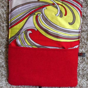 May include: A red and yellow patterned fabric pouch with a black zipper pull. The pouch is made of a soft, plush material and has a red fleece lining.