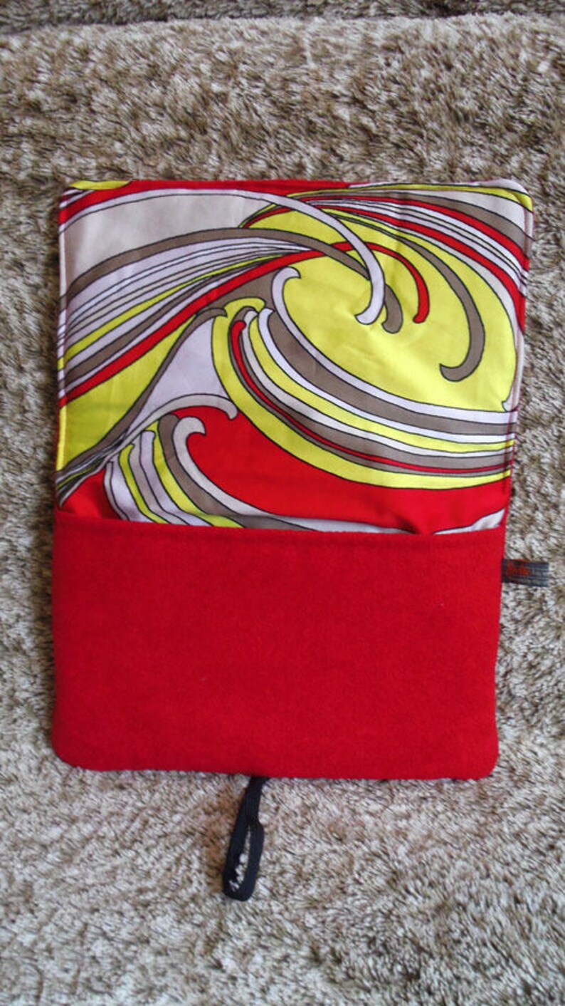 May include: A red and yellow patterned fabric pouch with a black zipper pull. The pouch is made of a soft, plush material and has a red fleece lining.