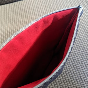 K&ouml;nnte beinhalten: Eine schwarze Rei&szlig;verschlusstasche mit rotem Futter. Die Tasche ist offen und das Futter ist sichtbar.