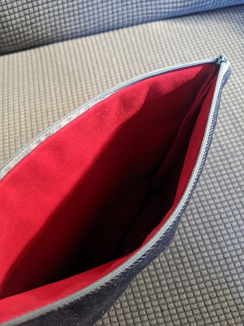 K&ouml;nnte beinhalten: Eine schwarze Rei&szlig;verschlusstasche mit rotem Futter. Die Tasche ist offen und das Futter ist sichtbar.