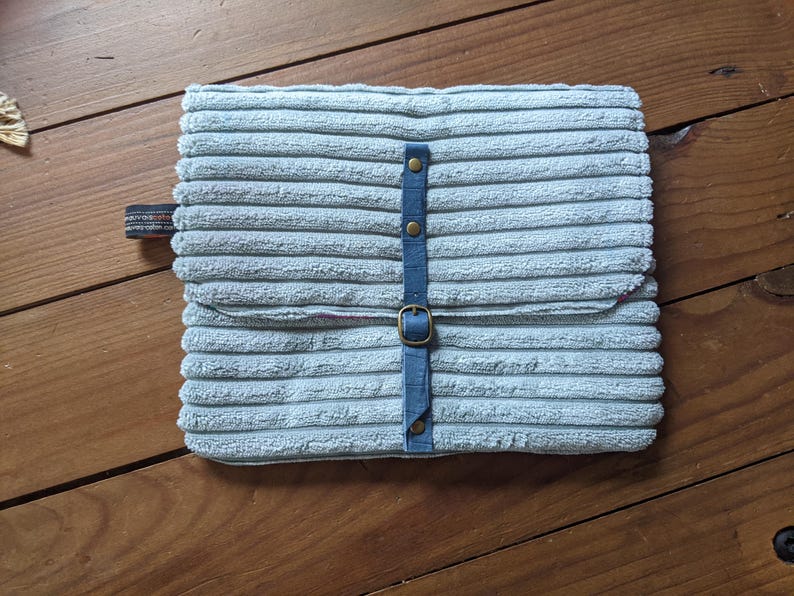 K&ouml;nnte beinhalten: Eine hellblaue Cord-Laptoptasche mit einem blauen Riemen und Messing-Schnallen.