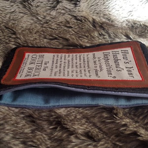 May include: A brown leather zippered pouch with a white fabric patch that reads "The New Butterick Cook Book" and a brown leather patch with white text that reads "How's Your Husband's Disposition? Is he irritable, moody, hard to please? You feel discouraged, hurt-but it is probably all your own fault! Disposition depends largely on digestion-you don't cook him well-balanced meals. Fats, vitamins, carbohydrates, proteins, minerals-all of them are needed to keep the human machine in good running order. Valuable facts on nutrition are given you in..."