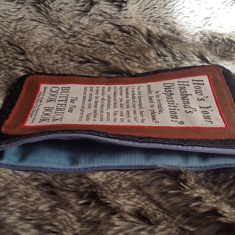 May include: A brown leather zippered pouch with a white fabric patch that reads "The New Butterick Cook Book" and a brown leather patch with white text that reads "How's Your Husband's Disposition? Is he irritable, moody, hard to please? You feel discouraged, hurt-but it is probably all your own fault! Disposition depends largely on digestion-you don't cook him well-balanced meals. Fats, vitamins, carbohydrates, proteins, minerals-all of them are needed to keep the human machine in good running order. Valuable facts on nutrition are given you in..."