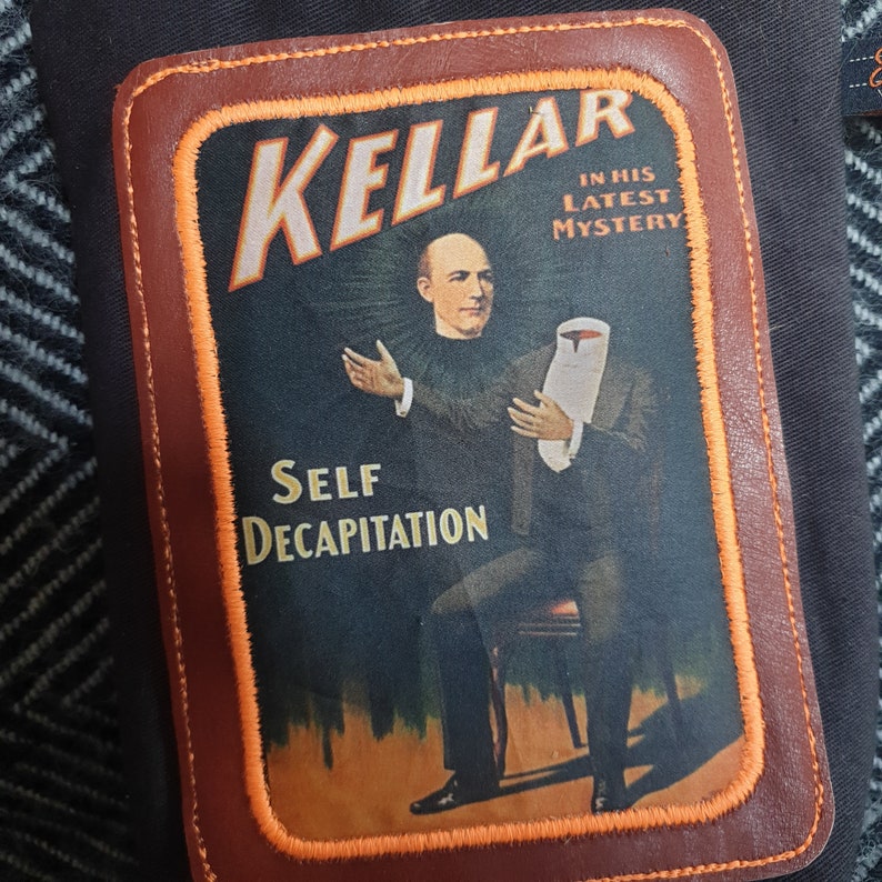 Pu&ograve; includere: Un poster in stile vintage che pubblicizza un mago di nome "Kellar" che presenta il suo ultimo mistero, "Self Decapitation". Il poster presenta un uomo in abito e cravatta che tiene un panno bianco sulla testa, su uno sfondo rosso con un bordo arancione.