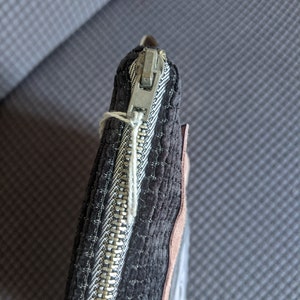 May include: A black quilted zipper pouch with a silver zipper. The pouch has a brown suede trim.