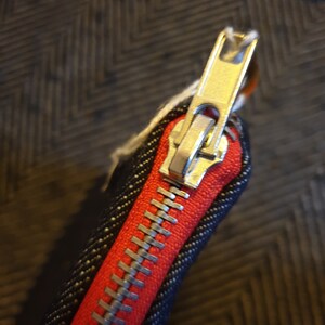 May include: A close-up of a red zipper with a silver zipper pull. The zipper is on a black and blue fabric.
