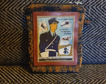 May include: A brown leather zippered pouch with a vintage-style patch featuring a French police officer and the text "POLICE NATIONALE LA POLICE, UN METIER D'HOMME RECRUTEMENT DE GARDIENS DE LA PAIX".
