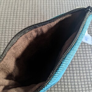 May include: A small, blue zippered pouch with a brown fabric lining. The pouch is made of a textured fabric with a subtle pattern.
