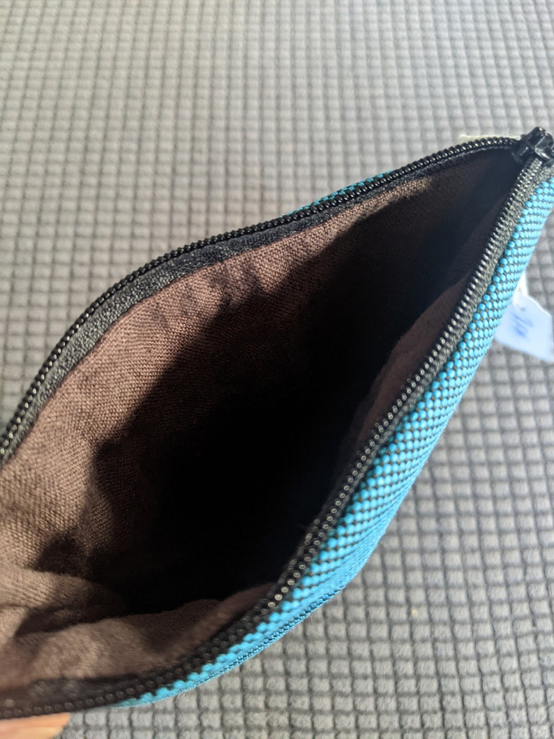 May include: A small, blue zippered pouch with a brown fabric lining. The pouch is made of a textured fabric with a subtle pattern.