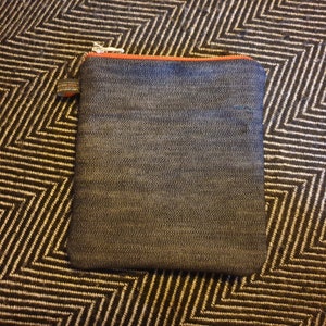 May include: A small, dark blue denim zippered pouch with an orange zipper pull. The pouch is lying on a black and white patterned surface.