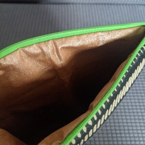 May include: A black and white striped zippered pouch with a green zipper and a brown fabric lining.