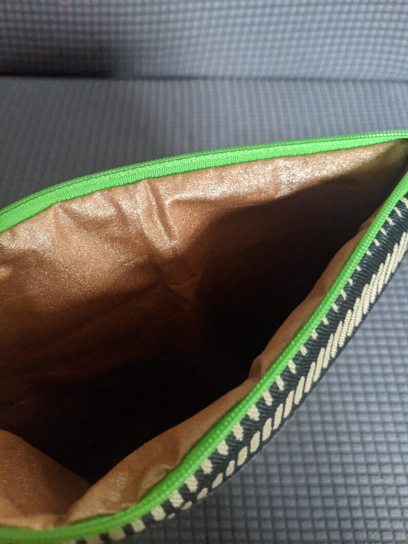 May include: A black and white striped zippered pouch with a green zipper and a brown fabric lining.