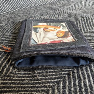 May include: A black denim zippered pouch with a rectangular window featuring a vintage photo of a woman with a red and white scarf. The pouch has a black zipper and a brown label with the word "Genuine" printed on it.