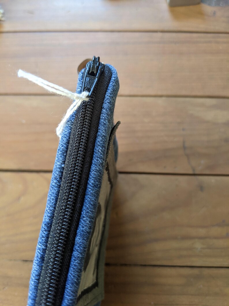 May include: A blue denim zippered pouch with a black zipper and a clear plastic window.