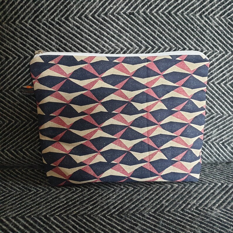 May include: A zippered pouch with a geometric pattern in shades of black, beige, and pink. The pattern is made up of triangles and squares.