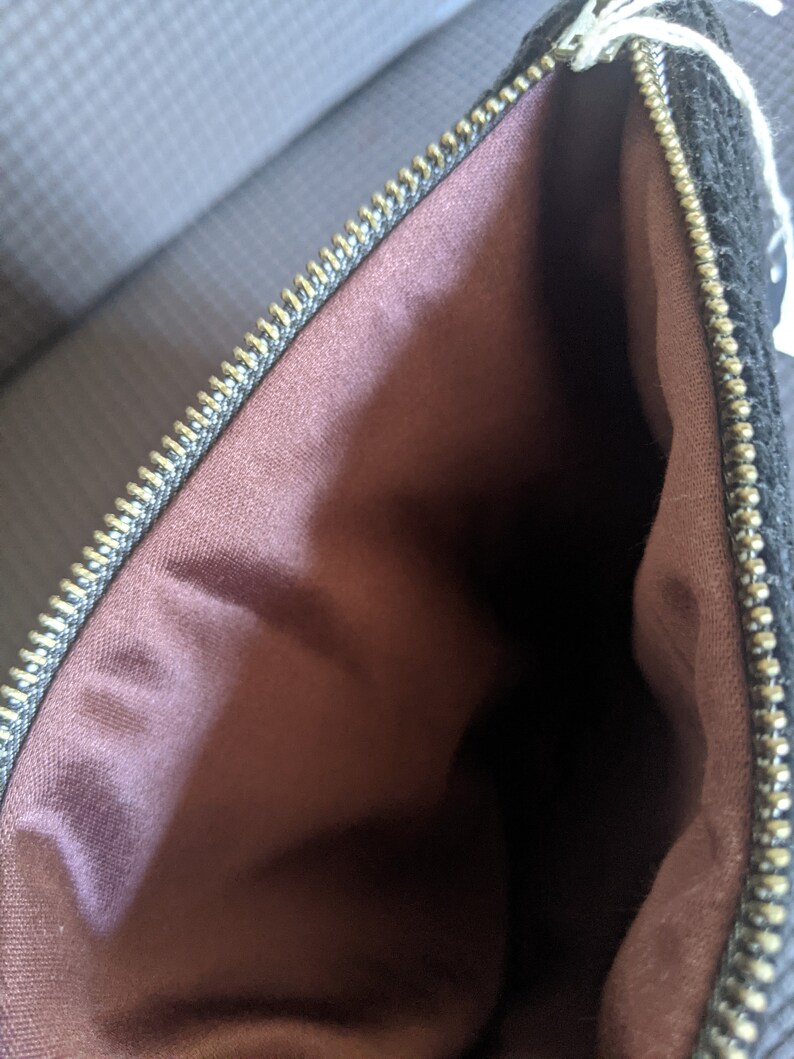 May include: A black zippered pouch with a brown fabric lining. The zipper is gold colored.