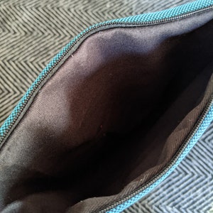 K&ouml;nnte beinhalten: Das Innere einer tealblauen Rei&szlig;verschlusstasche mit schwarzem Futter. Die Tasche ist aus einem weichen, strukturierten Stoff.
