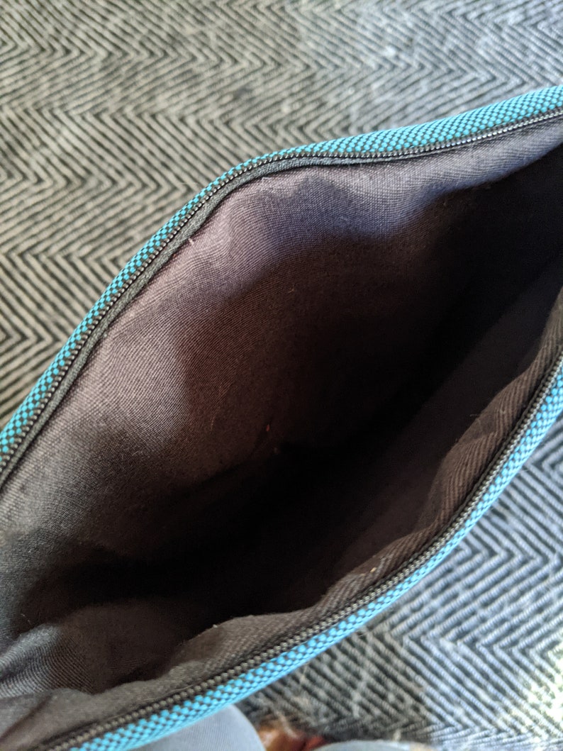 K&ouml;nnte beinhalten: Das Innere einer tealblauen Rei&szlig;verschlusstasche mit schwarzem Futter. Die Tasche ist aus einem weichen, strukturierten Stoff.