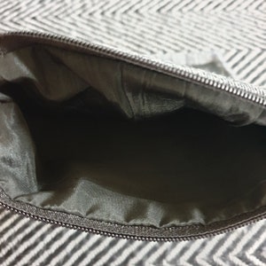 May include: A black zippered pouch with a black lining. The pouch is open and empty.