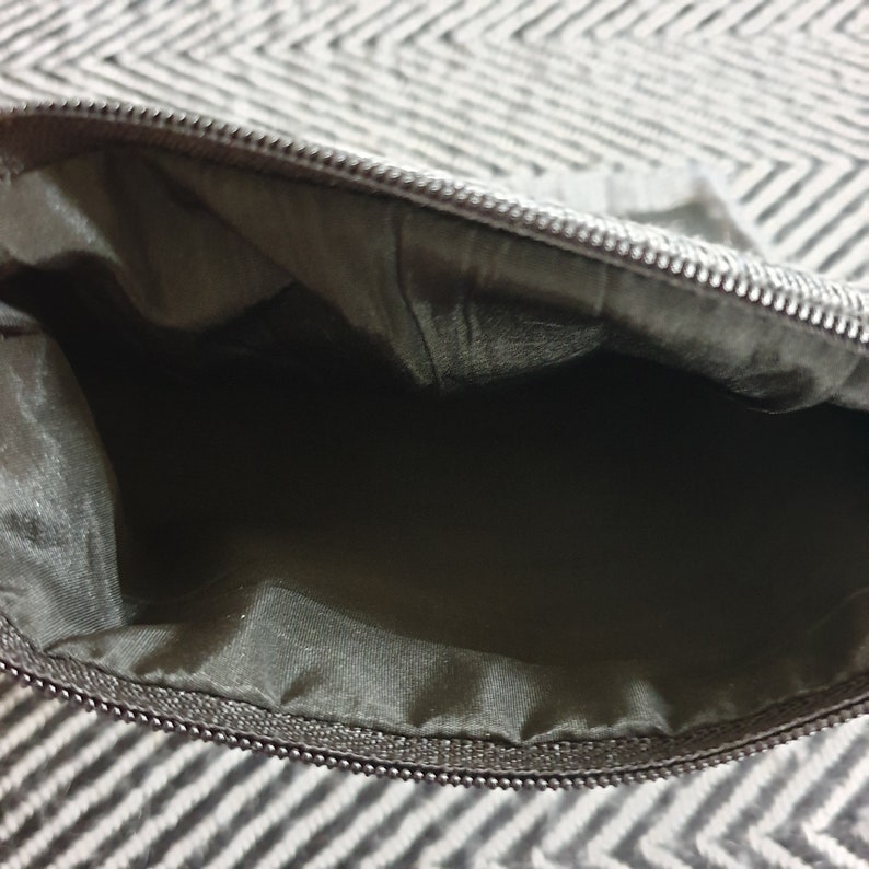 May include: A black zippered pouch with a black lining. The pouch is open and empty.