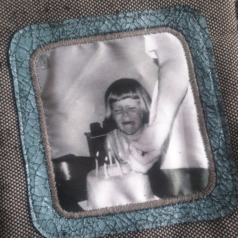 May include: A black and white photo of a young girl crying while blowing out candles on a birthday cake. The photo is framed in a blue and gray border.