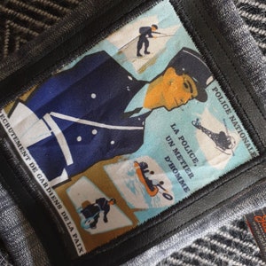 May include: A blue and white patch with a police officer illustration and the text "POLICE NATIONALE", "LA POLICE, UN METIER D'HOMME", and "ECRUTEMENT DE GARDIENS DE LA PAIX".