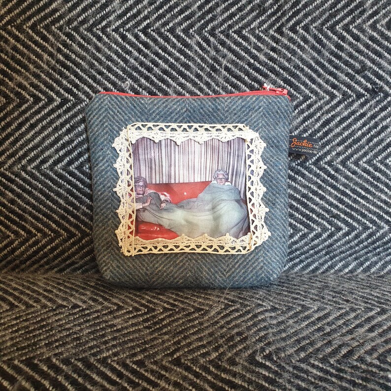 May include: A blue zippered pouch with a white lace frame around a vintage photo of two people under a blanket. The pouch has a small black tag with the text "Jackie's" on it.