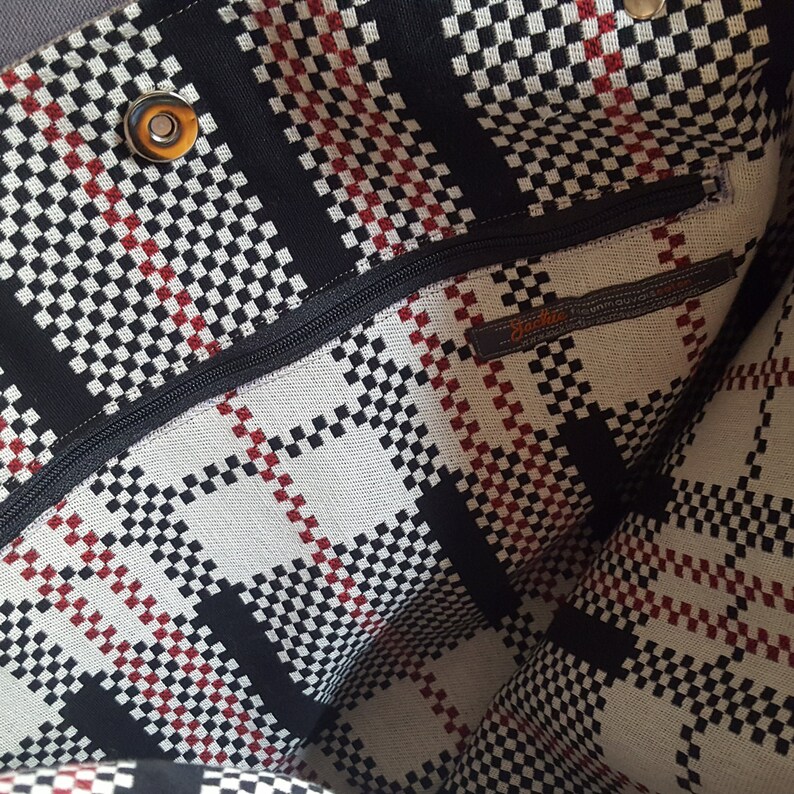 May include: The inside of a black and white checkered tote bag with a red stripe. The bag has a zipper closure and a label that reads "Jackie Unique".