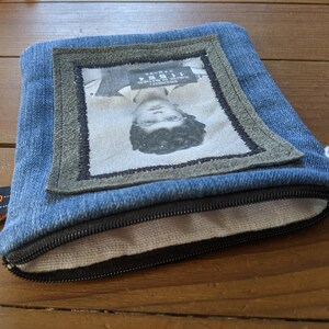 May include: A blue denim zippered pouch with a fabric lining. The pouch features a framed image of a person's face with a mugshot style photo and text that reads "WANTED".