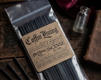 Peut inclure: Un sachet transparent contenant des bâtonnets d'encens noirs avec une étiquette marron. L'étiquette indique "Coffin Lining" et "Incense" avec la marque "Blackthorne & Co." et le texte "10 sticks". Une petite bouteille en verre est visible.