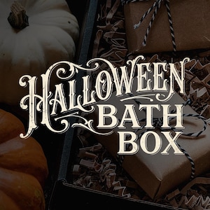 May include: A black gift box filled with brown paper packaging, tied with black and white twine, and surrounded by white and orange pumpkins. The text HALLOWEEN BATH BOX is printed in a decorative white font across the centre of the image.