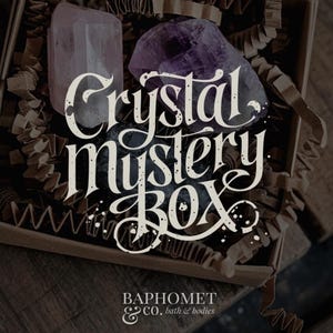 May include: A cardboard box containing crystals and packaging. The box features a large, pale purple crystal, a dark purple crystal, and a black crystal. The text "Crystal Mystery Box" is written in white script.