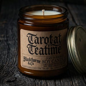 May include: A 227g soy candle in an amber glass jar with a metal lid. The tan label features black text reading Tarotat Teatime, Blackthorne & Co., Hand-Poured Soy Candle, Vegan, and Made in Canada, with safety instructions included.